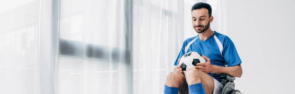 panoramic shot of man in football uniform sitting in Wheelchair and holding soccer ball - Valokuva, kuva