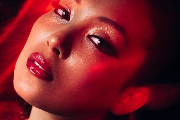 κοντά στο ελκυστικό αισθησιακό ασιατικό κορίτσι με το μακιγιάζ στο κόκκινο φως  - Φωτογραφία, εικόνα