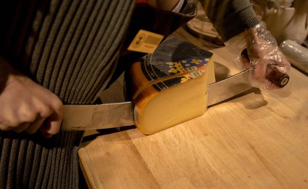 The seller cuts the cheese in the cheese shop. A large knife for - Foto, imagen