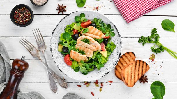 Salad with chicken fillet, olives, tomatoes and avocados in a plate on a wooden background Top view. Free space for your text. Flat lay - Fotografie, Obrázek