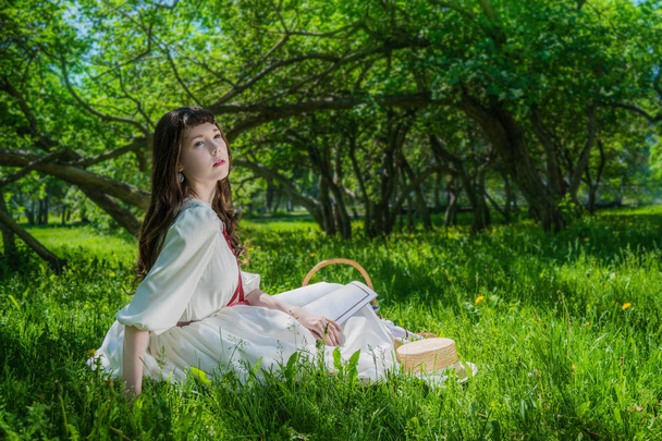 Woman in a white dress sitting under a tree lilacs. - Zdjęcie, obraz