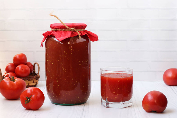 El jugo de tomate en latas y en un vaso está sobre la mesa sobre un fondo blanco
 - Foto, Imagen