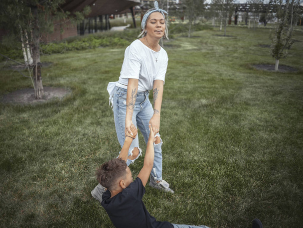 Young pretty mum whirling with her son at park. Happy family concept. - Φωτογραφία, εικόνα