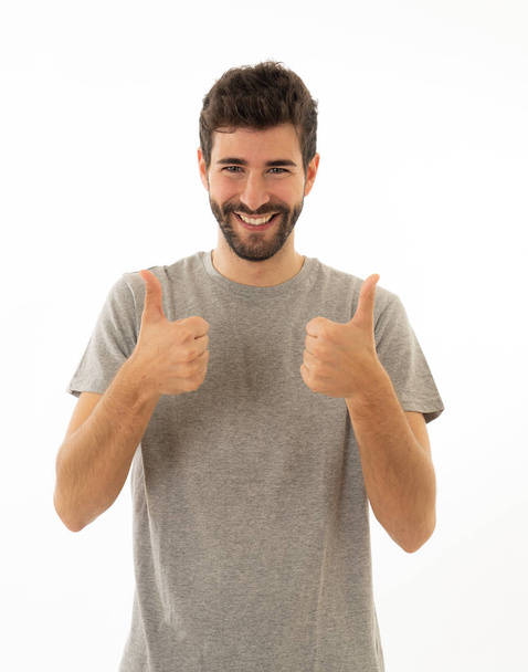 Portrait of good looking young man showing thumbs up sign feeling cheerful, happy and satisfied. Young happy student male making thumb up in joyful approval gesture isolated on white background. - Foto, afbeelding