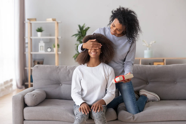 African American mother closing eyes of teen daughter, preparing surprise - Zdjęcie, obraz