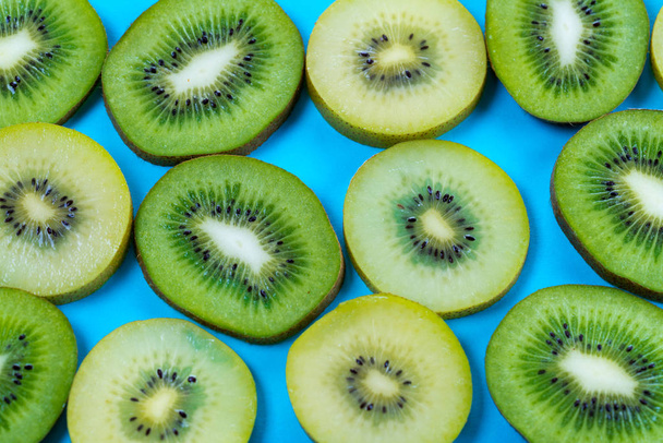 horizontal view of slices of golden yellow and green kiwi fruit on a bright high contrast turquoise background - Photo, Image