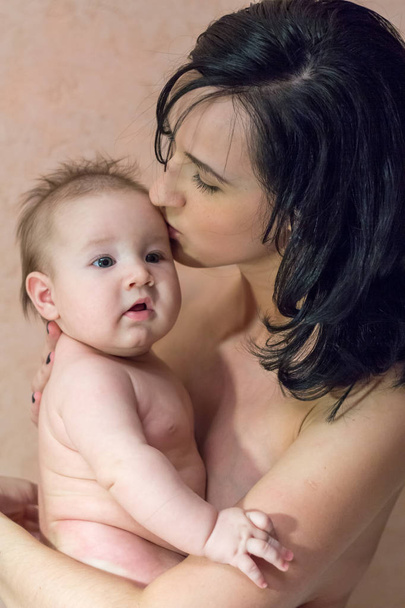 junge schöne Mutter Brünette ohne Kleidung hält ihre Arme und küsst ihren kleinen Sohn - Foto, Bild