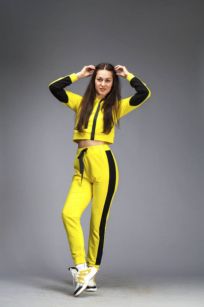 Portrait of a young beautiful brunette woman in yellow tracksuit - Фото, изображение