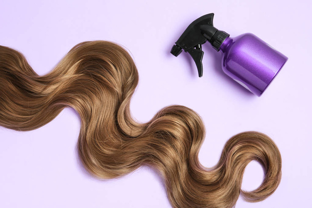 Lock of brown wavy hair and spray bottle on color background, flat lay - Фото, зображення