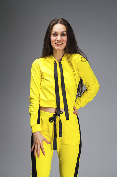 Portrait of a young beautiful brunette woman in yellow tracksuit - 写真・画像