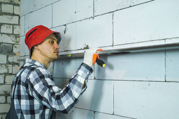 young man in work wear checking straightness of block wall with bubble level - Photo, Image