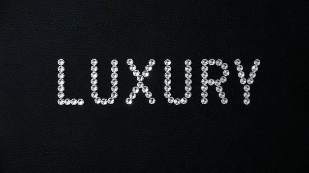 Slovo luxus z lesklých bílých krystalů swarovski umístěných na černé kůži - Fotografie, Obrázek