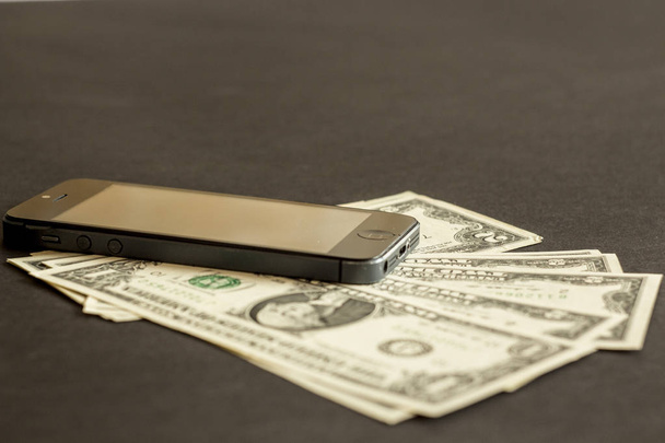 dinheiro de papel e um telefone celular deitado em um fundo preto
 - Foto, Imagem
