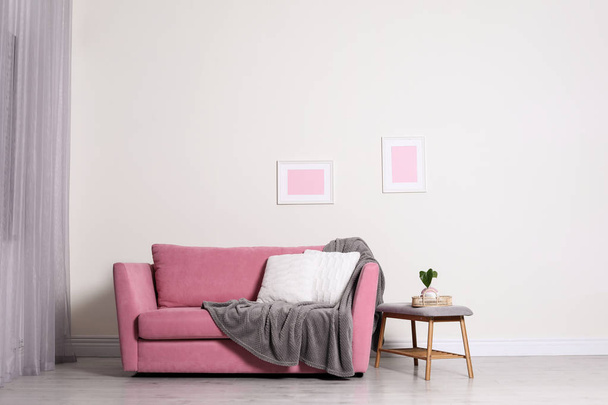 Cozy living room interior with sofa, pillow and plaid near light wall. Space for text - 写真・画像