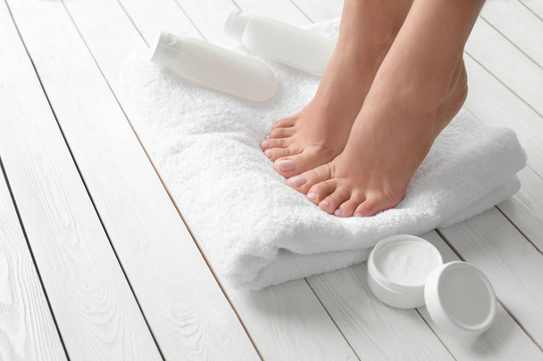 Woman with beautiful feet, towel and cosmetic products on white wooden floor, closeup. Spa treatment - 写真・画像