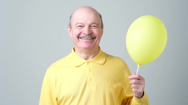 Starší muž se žlutým balonem s héliem v ruce - Záběry, video