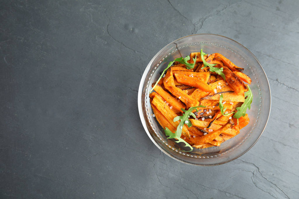 Glass bowl with baked sweet potato slices and arugula on grey background, top view. Space for text - Foto, afbeelding