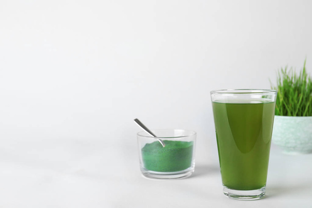Glass of spirulina drink and bowl with powder on white background. Space for text - Fotó, kép