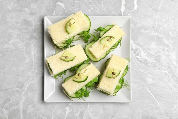 Plate with traditional English cucumber sandwiches on grey background, top view - Фото, изображение