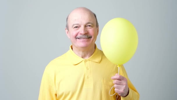 Senior man with yellow balloon with helium in hand - Кадры, видео