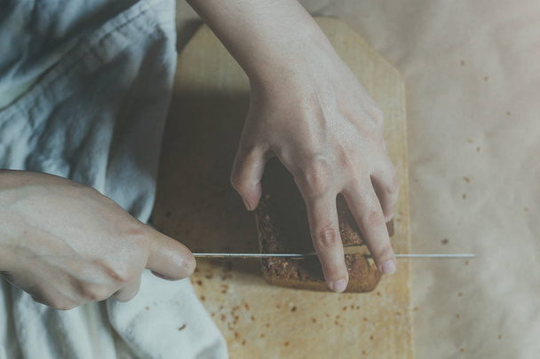 Dona de casa a cortar um pão. Pão de corte feminino na tábua de corte. Vista de cima. Vista superior de pães
 - Foto, Imagem