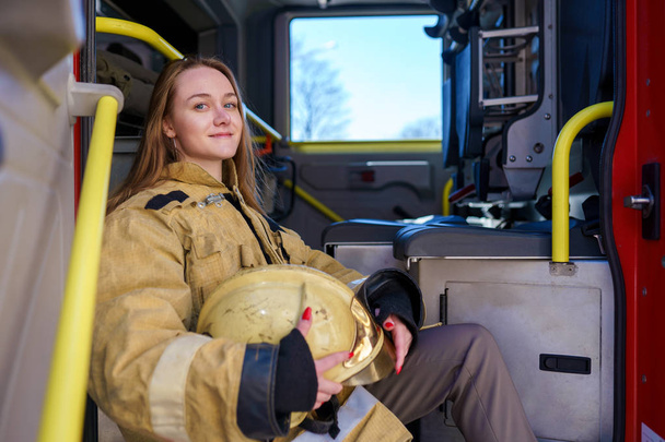 Фото щасливої пожежної жінки, що стоїть на пожежній машині
 - Фото, зображення