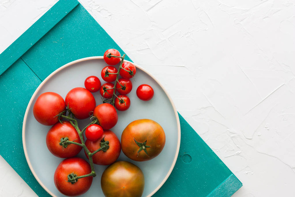Different types of tomatos on white plate, turquoise tray and white background with space for text message - Foto, Imagen