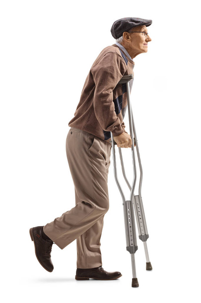 白い背景に隔離された松葉杖で歩く先輩男性の全長プロフィールショット - 写真・画像