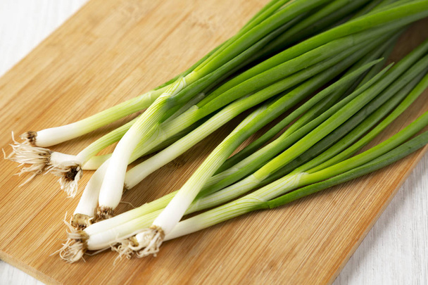 Fresh green onions on a bamboo board on a white wooden surface,  - Photo, Image