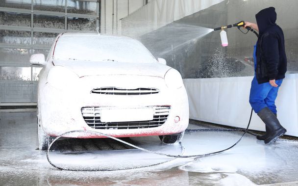 Worker cleaning automobile with high pressure water jet at car wash - Fotó, kép
