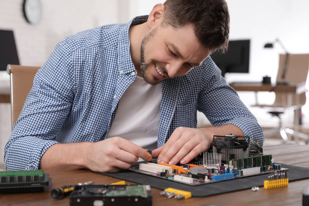 Male technician repairing motherboard at table indoors - Foto, Bild