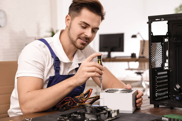 Male technician repairing power supply unit at table indoors - Photo, Image