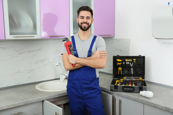Male plumber with pipe wrench in kitchen. Repair service - Foto, afbeelding
