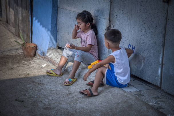 SIHANOUKVILLE, CAMBODIA - FEVEREIRO 25, 2019: Cena de irmão e irmã tocando no corredor de sua casa na vila de pesca de Sihanoukville
 - Foto, Imagem