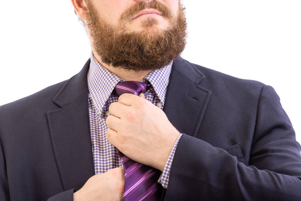 Nahaufnahme Porträt eines großen gutaussehenden bärtigen Geschäftsmannes in einem dunklen Anzug richtet hellblaue Krawatte, isoliert auf weiß - Foto, Bild