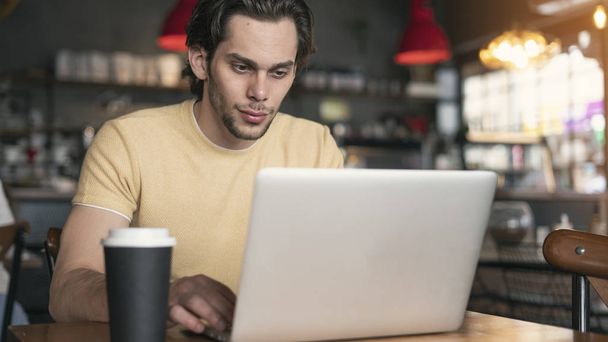 Młody człowiek korzystający z laptopa w kawiarni - Zdjęcie, obraz