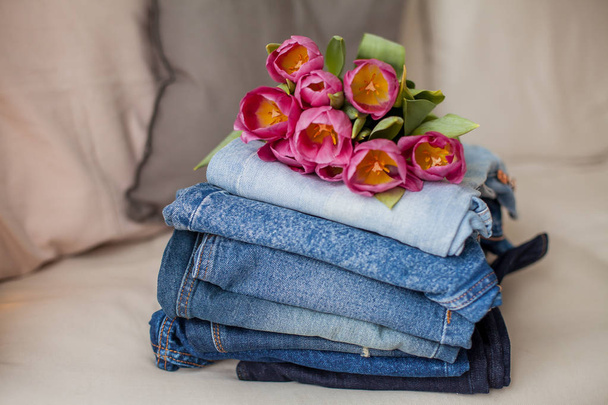 Nahaufnahme. Ein Strauß Tulpen liegt auf einem Haufen Jeans. Kleidung. - Foto, Bild