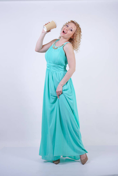 bonita loira caucasiano mulher vestindo longo azul verão vestido segurando xícara de papel de café e goza de vida no estúdio branco fundo
 - Foto, Imagem