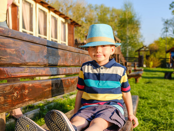 Smiling child sitting on a park bench with green meadow on background - Foto, imagen