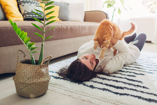 junge Frau spielt mit Katze auf Teppich zu Hause. Herrchen liegt mit Haustier auf dem Boden - Foto, Bild