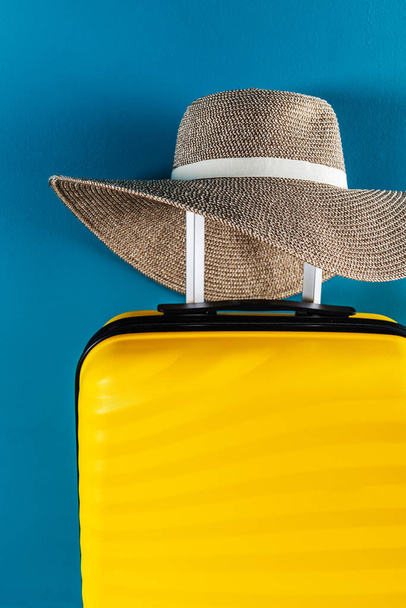 Φωτεινή και κομψή βαλίτσα μεγέθους καμπίνας με ψάθινο καπέλο - Φωτογραφία, εικόνα