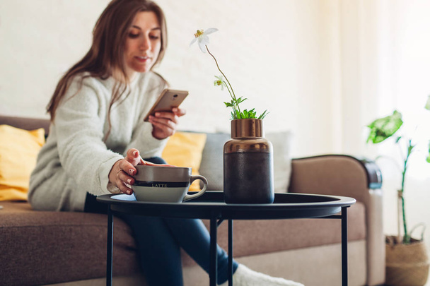 Jovem relaxante na sala de estar usando smartphone e beber café. Decoração de interiores
 - Foto, Imagem