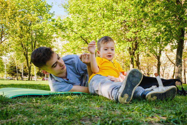 Cheerful two brothers lie on the grass in the park and play in funny games - Φωτογραφία, εικόνα