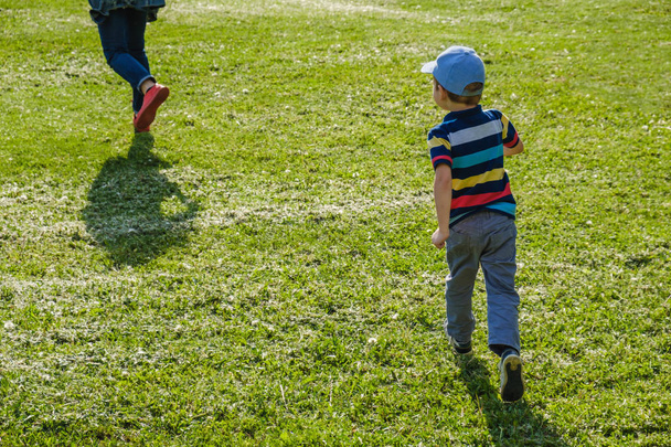 Young boy runs in a green field. Cute child running across park outdoors grass. - Foto, Imagem