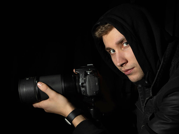 Uomo fotografo con una fotocamera DSLR su un treppiede in un cappuccio nero
  - Foto, immagini
