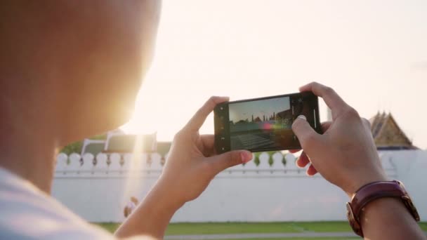 Traveler Asian man using mobile phone for take a picture while spending holiday trip at Bangkok, Thailand, male enjoy journey at amazing landmark in sunset. Lifestyle men travel in city concept. - Footage, Video
