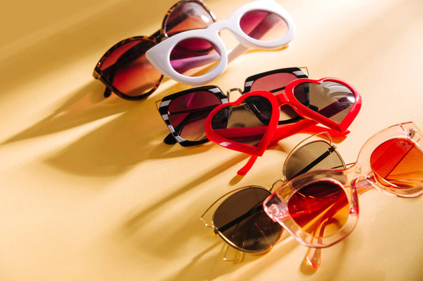 Set of Stylish sunglasses with bright sunlight on yellow background. Flat lay, top view. Summer fashion concept - Valokuva, kuva