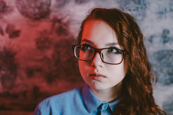 Retrato artístico de una hermosa chica pelirroja con gafas rojas y una camisa azul. Piercing en el labio
. - Foto, Imagen
