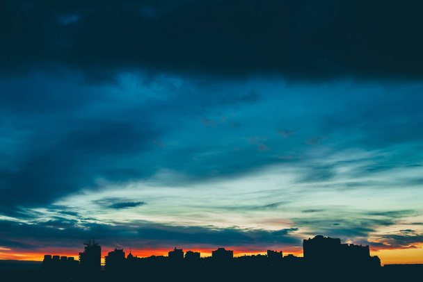 Міський пейзаж з чудовим різнокольоровим яскравим світанком. Дивовижне різнокольорове хмарне небо над темними силуетами міських будівель. Атмосферний фон сходу сонця в похмуру погоду. Копіювати простір
. - Фото, зображення