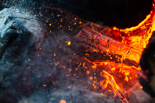 Gesmolten houtblokken verbrand in levendig vuur van dichtbij. Sfeervolle achtergrond met vlam van kampvuur. Onvoorstelbaar gedetailleerde afbeelding van vreugdevuur van binnenuit met kopieerruimte. wervelwind van rook en gloeiende vlammen. - Foto, afbeelding
